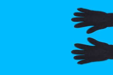 Obraz premium Pair of black warm woolen gloves on blue background with copy space for your text. Top view