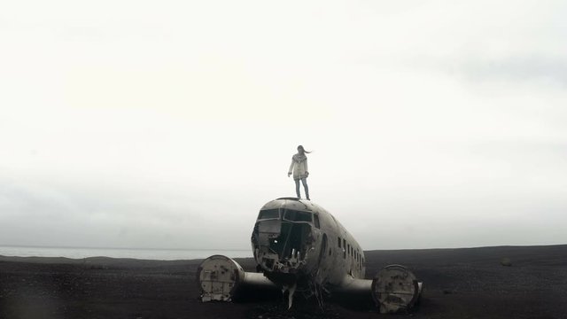 Young traveling woman standing on the top of breaker DC-3 BMC plane on the black beach in Iceland. Hair waves on wind.
