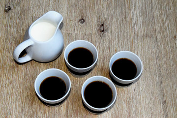 Four cups of coffee and milk pot on wooden table