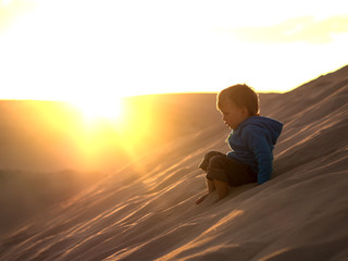 Fototapeta na wymiar Adorable little boy sliding down the desert dune