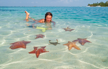 girl in shallow water of san Blas Island, surrounded by colorful seastars
