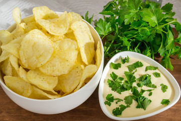 Crispy potato chips and fresh mayonnaise with parsley in a white bowls on a table. Fast food and tasty snack consept