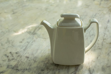 white shiny ceramic teapot stands on a light, blurred marble tabletop