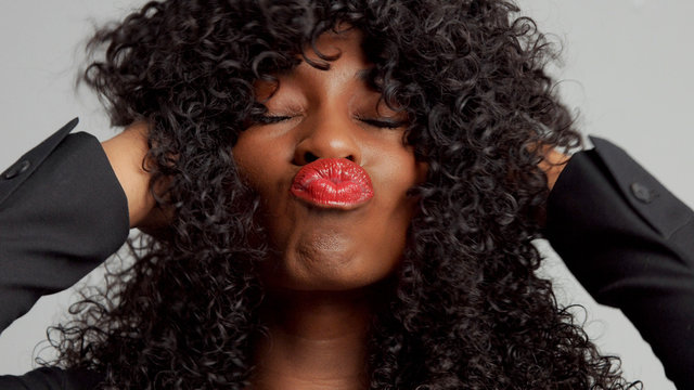 black woman with curly black hair sending kiss to the camera. Red lips kiss