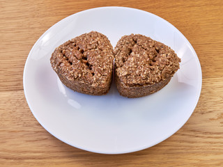 A white plate standing on a wooden table on which there are Two slices of homemade bread.