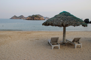 Empty sun loungers and bamboo parasol on the tropical sea overlooking the rocks at sunset