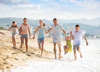 Family with four kids happily running on beach