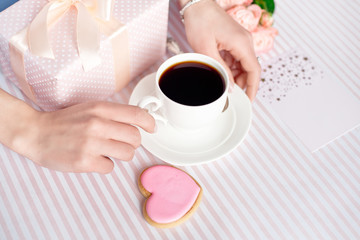 Mother's day concept - a gift for women hands with a white cup of coffee and roses. Copy space.