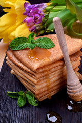 Fototapeta na wymiar Stack of crepes topped with honey and mint on a black wooden board