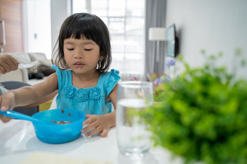 cute asian toddler having breakfast by herself at home in the morning