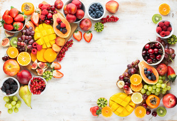 Healthy raw fruits background, cut mango papaya, strawberries raspberries oranges plums apples kiwis grapes blueberries cherries, on white table, copy space, top view, selective focus