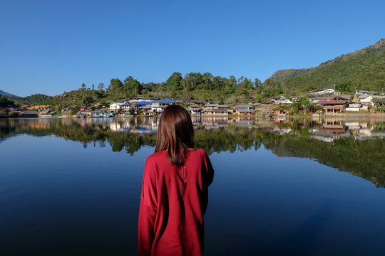 asia women traveller stand near reflect lake looking out to view of old house at ban ruk thai Mae Hong Son Thailand
