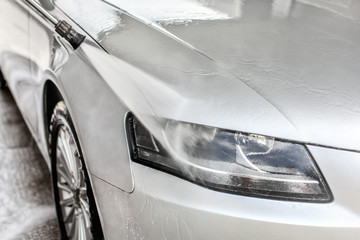 Silver car front light washed in self serve carwash. Detail of water jet stream spraying on glass...