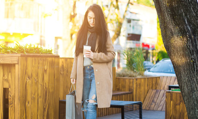Woman walking with shopping bag and hot coffee in city center