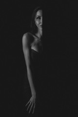 alluring sexy woman in evening dress posing over dark background. black and white