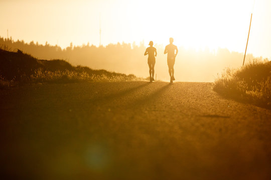 A male and female runner running dusty backlit rural roads in the Palouse region of north Idaho and eastern Washington at sunset.   