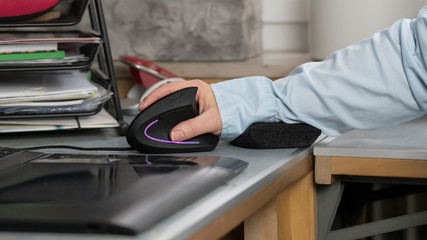 Ein Arbeitsplatz mit Computer. Auf dem Schreibtisch ist eine Hand in entlastender Position mit einer ergonomischen Maus. ein kleines Kissen  unterstützt das Handgelenk. Gesundheits Prävention. - obrazy, fototapety, plakaty