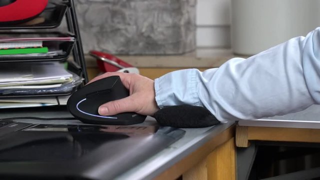 Ein Arbeitsplatz mit Computer. Auf dem Schreibtisch arbeitet eine Hand in entlastender Position mit einer ergonomischen Maus. Ein kleines Kissen unterstützt das Handgelenk. Echtzeit mit Ton.