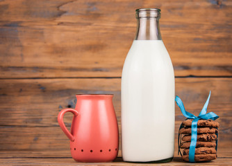 Bottle of milk, pink mug and cookies with chocolate chips on wooden background.Village Breakfast