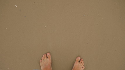 The legs of a man go slowly along bare sand on a golden sandy beach.