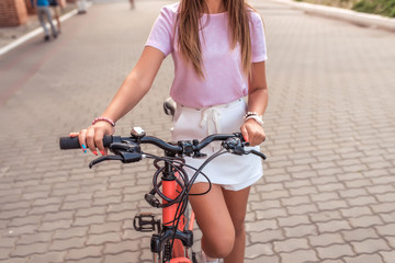 Naklejka premium A girl stands with a bicycle in summer in the city. Close-up steering wheel and brakes, with a security secret lock on the frame. Woman in casual clothes.
