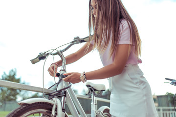A girl stands with a bicycle in summer in city. In hands of a lock with a code, it closes and protects its transport against theft. The concept of protection against theft and thieves of bicycles.