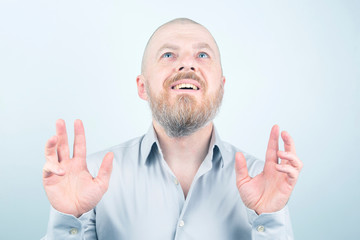 Portrait of happy bearded man with raised hands on light background.