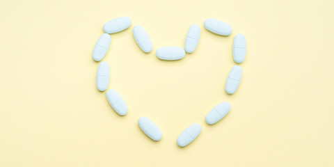 Blue pills forming heart shape on pastel yellow