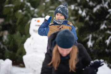 Little boy throwing a snowball at his mother