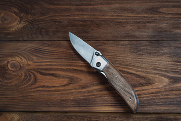 hunting bowie knife with a wooden handle on dark wooden background. Steel arms weapon.