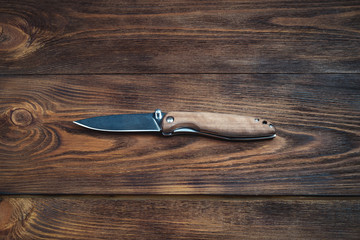 hunting bowie knife with a wooden handle on dark wooden background. Steel arms weapon. top view