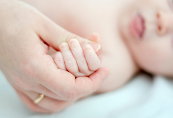 the little baby lies on her back and holds the mom's hand with the little wrinkled handle. light key