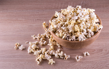 popcorn in a wood cup and on a wood table at a dark background