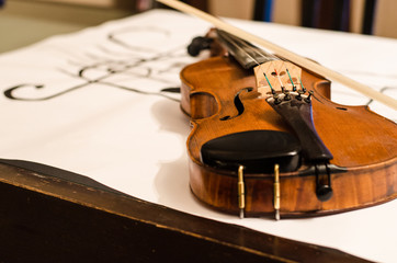 Close up of Violin body with bow positioned in a diagonal over a musical stave drawing with a G-clef with musical notes on a white background