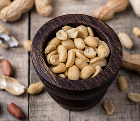 Peanuts in small dark wooden bowl on natural rustic desk.