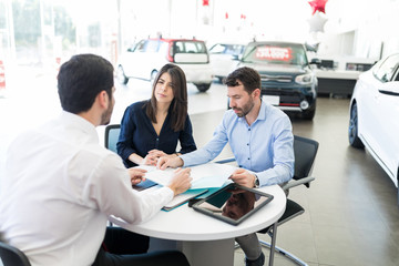 Mid Adult Couple And Seller With Car Purchase Terms