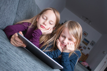 2 girls lie on the sofa and look happily at the screen of a tablet