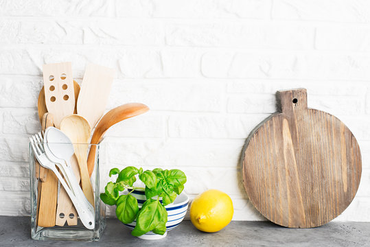 Kitchen tools, olive cutting boan a kitchen shelf against a white brick wall. Fresh basil and lemon. White and black modern cutlery. No plastic house