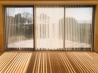 sunlight shining through full length white vertical blinds in front of three glass sliding french...