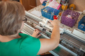 A woman knits on a knitting machine, working with her hands