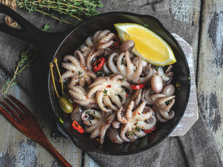 Baby octopus cooked, roasted in the iron pan portion, with lemon and seasoning close up © koss13
