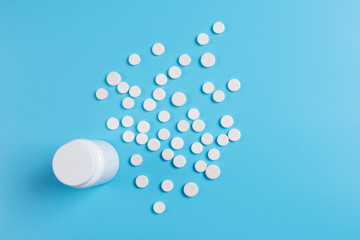 White pills, tablets and white bottle on blue background.