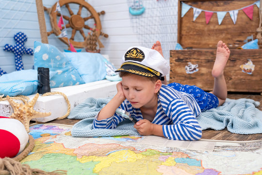 little boy in the image of a sailor playing in his room. examines through a magnifying glass card