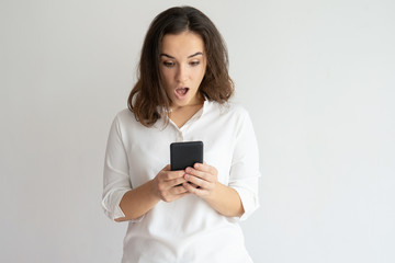 Naklejka premium Shocked woman holding smartphone and looking at its screen