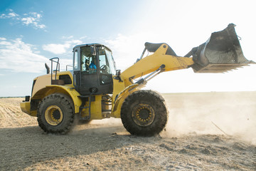 Yellow tractor on the golden sunrise, with a raised working organ