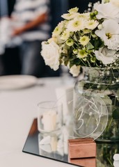 The wedding table decoration with mirror stand, glass table number and vase with flowers 