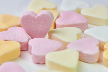 macro color photo of candy hearts lying on white background, one pink heart is standing, copy space