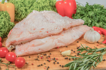 Raw fat with pigs on a wooden board with cherry tomatoes, lettuce leaves, garlic, chilli pepper, rosemary, onion