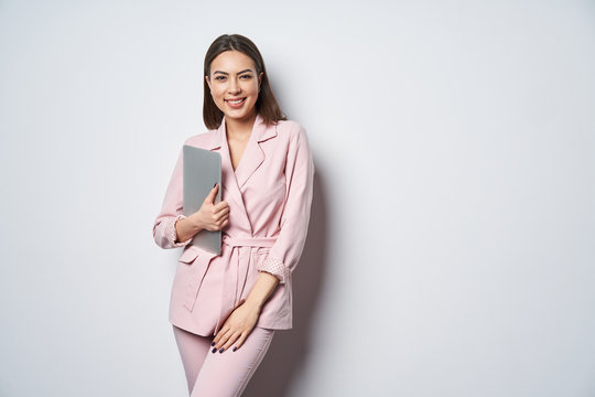 Confident business woman wearing pink suit with laptop underarm