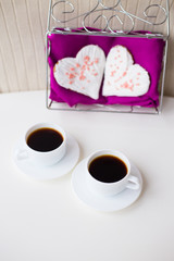 two cups of coffee and biscuits in the form of heart on a pink napkin